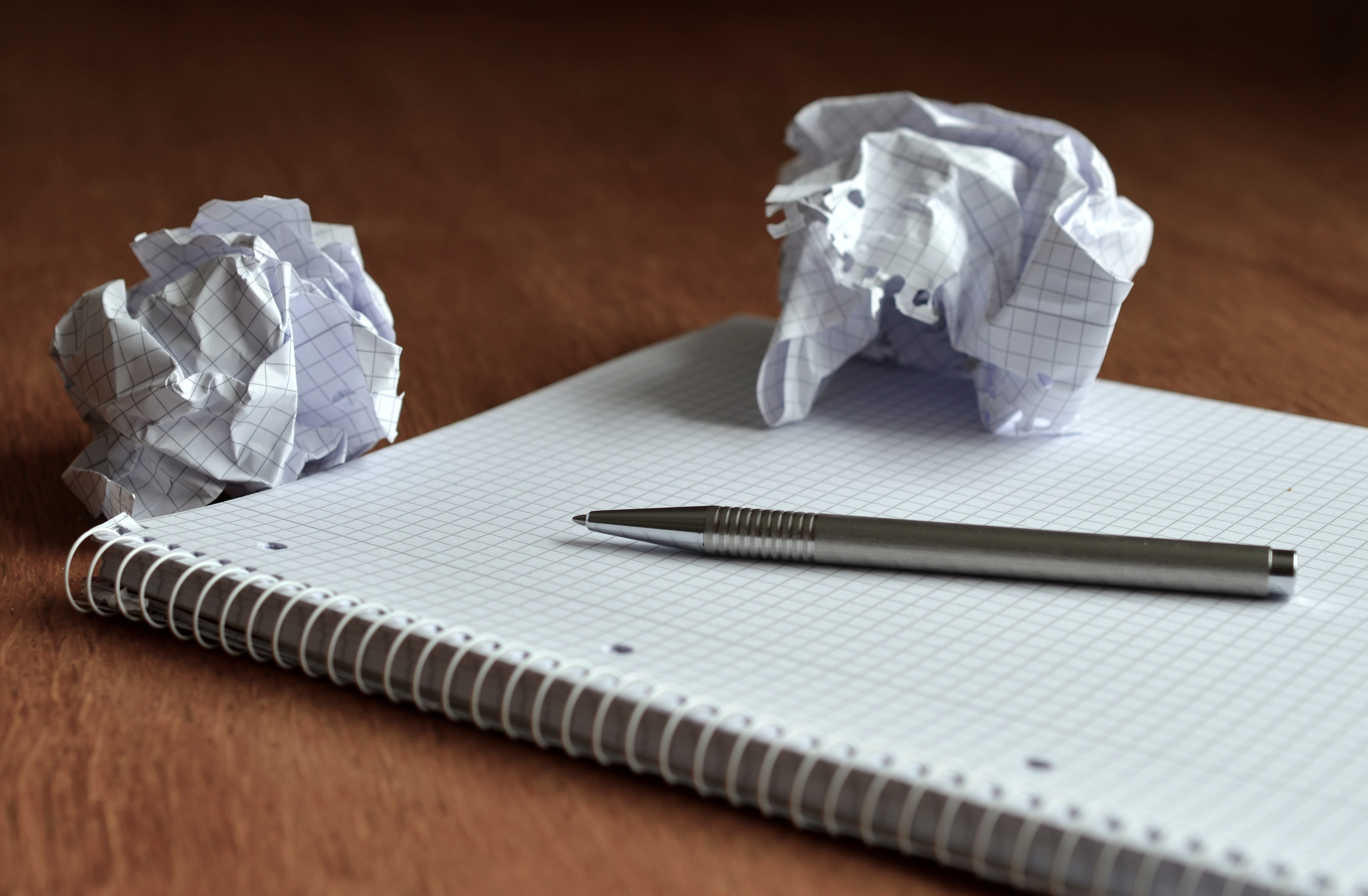 On voit un cahier boudiné à feuille cadrillée avec un crayon déposé en diagonale dessus. Deux boules de papiers froissés sont déposé au haut du cahier.
